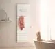 Vertikaler weißer Heizkörper von Kermi mit Längsrippen, an der Wand montiert. Ein Handtuch hängt daran, im Hintergrund ein Bad mit Wanne und Tageslicht.